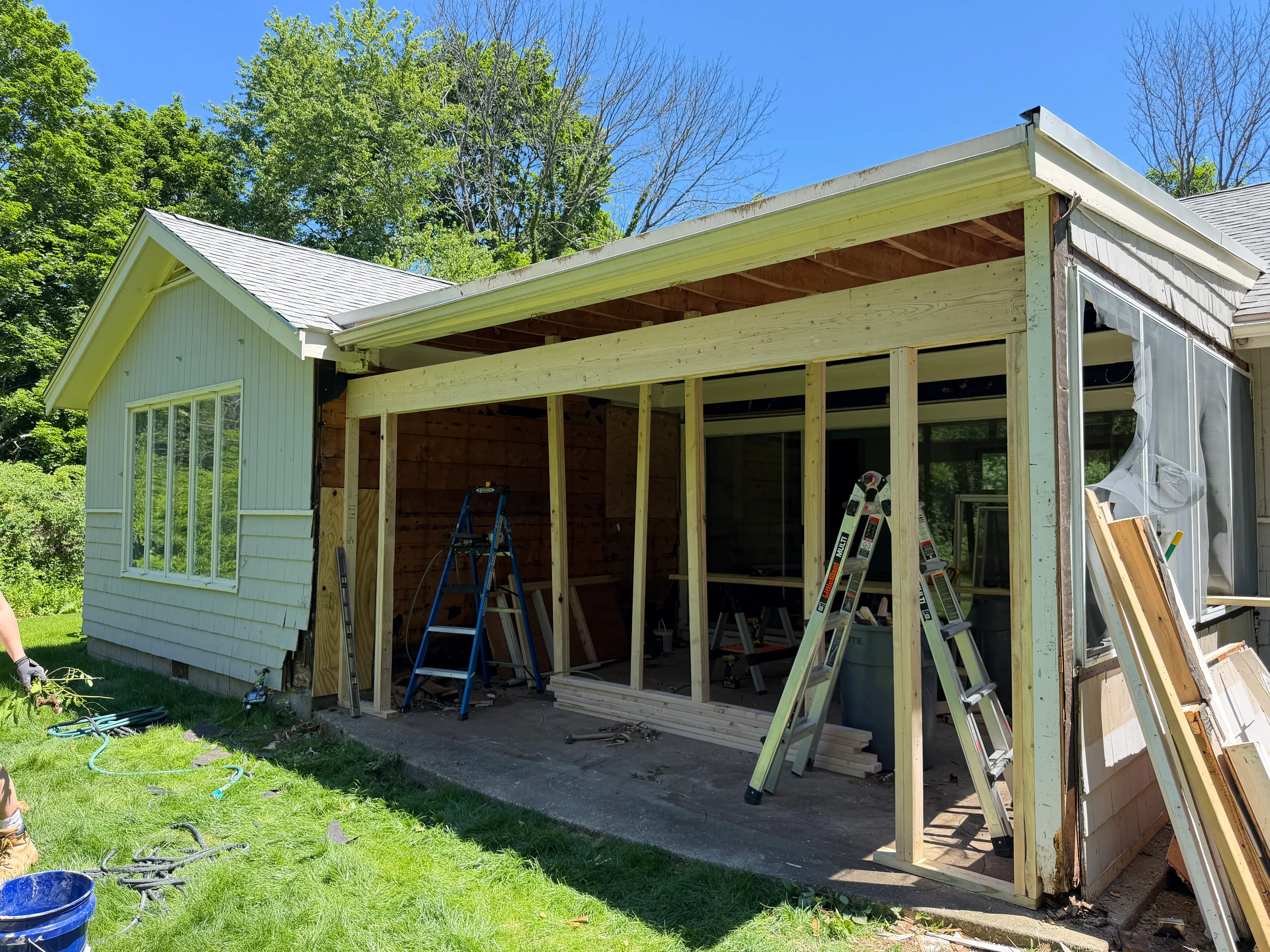 New roof framing and shingles on home addition with covered porch, mid-construction